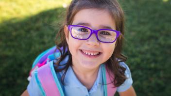 Young elementary girl wearing purple glasses and a backpack