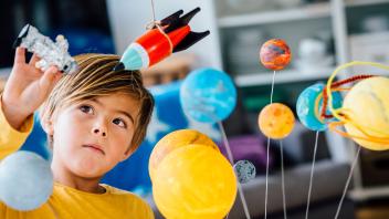 Young boy fascinated by models of a space rocket, astronaut and the planets
