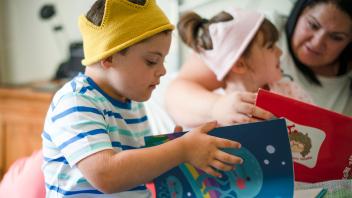 boy and girl wearing knit crowns looking at reading picture books with mother