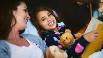 mother and daughter reading books together with stuffed animals
