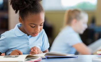 Elementary student reading book at her desk