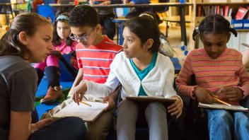row of elementary school kids talking with teacher about a reading assignment