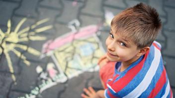 Young boy doing a sidewalk chalk drawing of sun and home