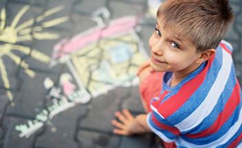 Young boy creating colorful chalk drawing outside