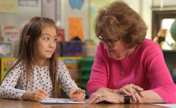 Reading tutor working with a first grade student at a desk