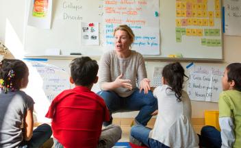 Second grade teacher giving an ELA lesson to small group of students sitting on the carpet.