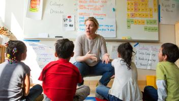 Second grade teacher giving an ELA lesson to small group of students sitting on the carpet.