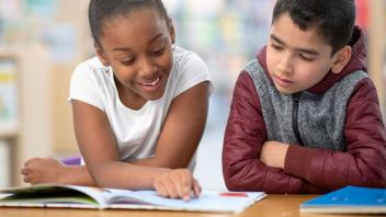 elementary student reading a picture book aloud to another student in class