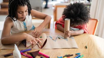 Two young kids at home creating things out of cardboard and markers
