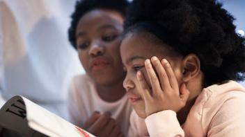 Young Black girl looking at picture book with her mother