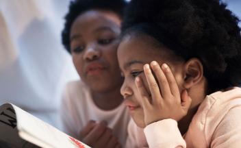 Young Black girl looking at picture book with her mother