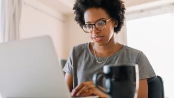 Young Black teacher looking at laptop at home