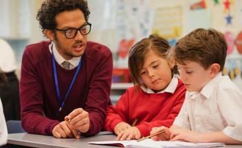 Male elementary teacher working with two students on a lesson