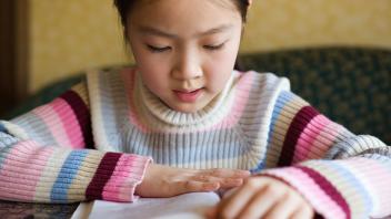 Elementary girl in colorful striped sweater reading a book
